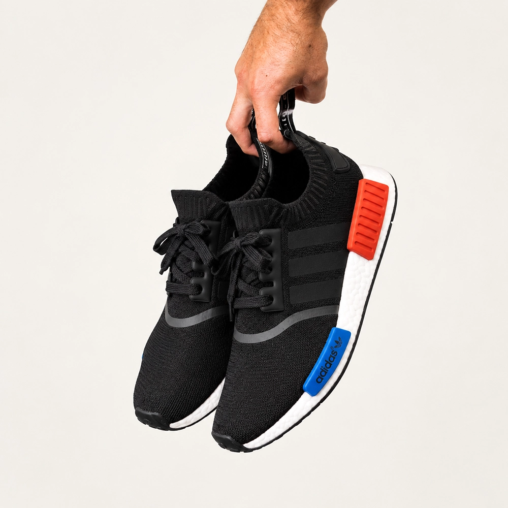 adidas NMD R1 經典黑白休閒運動鞋，黑色針織鞋面搭配白色中底、紅藍 EVA 穩定塊，雙鞋手提展示圖